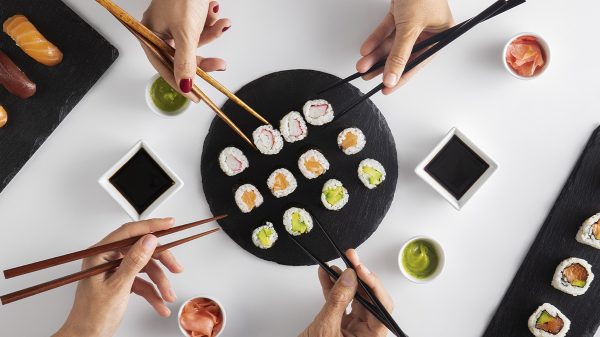 Hands grabbing sushi with chopsticks. Shared sushi platter with sauces and ginger.
