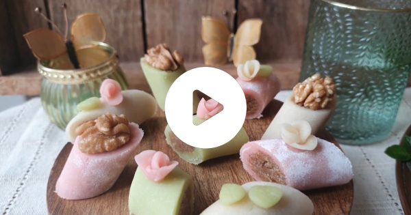 Sortido de doces decorados, com nozes, decorações florais e borboletas ao fundo.